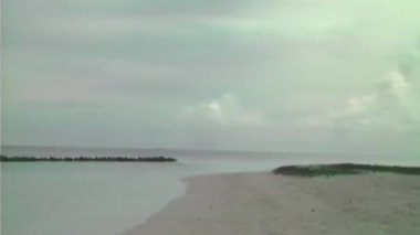 Güzel bir Maldivler plajı kıyı boyunca uzanan ince, açık renkli kumlara sahiptir, hafif dalgalarla sakin bir okyanusa yol açar, ufuk bulutlu gökyüzü ile kusursuz bir şekilde harmanlanır.