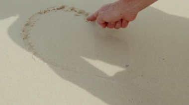Kumda çizilmiş bir kalp yavaşça gelen dalgalarla sürüklenir.