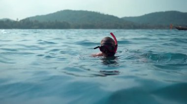 Sakin bir okyanus sahnesinde mavi sularda yüzen bir turist, hafif dalgalar ve güneşli deniz güzellikleriyle çevrili şnorkelle yüzüyor.