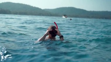 Krabis 'in sakin sularında yüzerken şnorkelini ayarlayan bir adam, güneşli yüzeyin altına dalmaya hazırlanıyor.