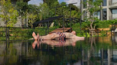 Bir adam havuzun kenarında uzanır, yavaşça kalkmadan önce güneşin altında güneşlenir, rahatlamanın tadını çıkarır.