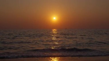 Yumuşak dalgalar, sakin deniz suyunda rüya gibi bir gün batımını yansıtarak huzurlu ve huzurlu bir manzara yaratır.