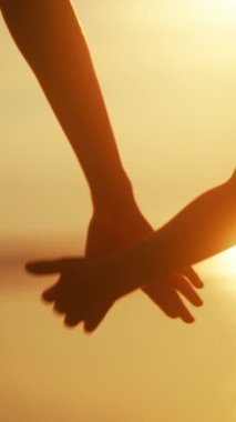 Kardeşlerin siluetli elleri, gün batımında canlı bir gökyüzüne karşı bir arada tutarak, bağı ve birlikteliği simgeliyor.