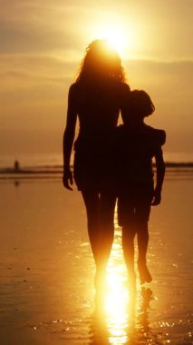 Bir erkek ve kız kardeş, gün batımının yumuşak ışığında ıslak kumda yürür. Abla, kardeşinin elini nazikçe tutmadan önce, kolunu omzuna sarar. Yürekten bir kardeş bağı kurar.