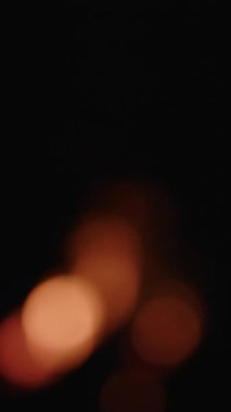 Yakın çekim, odak dışı çekim yanıp sönen alevleri yakalar, sıcak turuncu-kırmızı renkler koyu arkaplana karşı dramatik ve neredeyse ruhani bir etki yaratır.