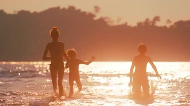 Çocuklar kıyı kenarında neşeli ve enerjik bir anın tadını çıkararak parıldayan okyanus dalgalarında koşup sıçrıyor.