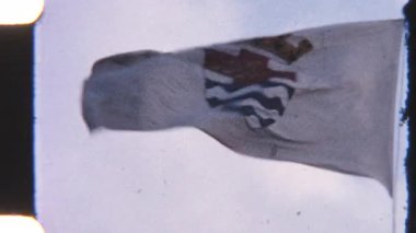 8 mm 'lik eski bir film, rüzgarda dalgalanan kraliyet arması olan beyaz bir bayrak yakalar. Hareketi, parçalı bulutlu bir gökyüzüne karşı uzun bayrak direği tarafından vurgulanır.