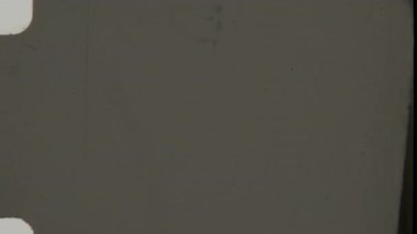 Klasik bir 8 mm 'lik film, eski film stoklarının görünümünü çağrıştıran zayıf çizikler, yıpranmış kenarlar ve ince kusurlarla dolu septik tonlu bir arka plan içerir.