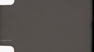 Hafif tahıl, hafif toz zerreleri, yumuşak vignette kenarları, klasik sproket delikleri ve ince bir klasik estetik çağrıştıran hafifçe kararmış sınırları içeren temiz ve minimal bir 8 mm 'lik film.