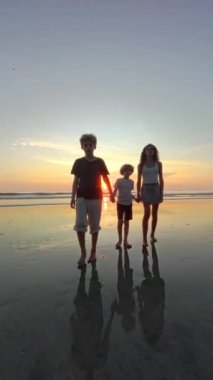 Gün batımında kumsalda el ele yürüyen çocukların 360 'lık görüntüsü. Güneş arkalarında batarken huzurlu bir anın tadını çıkarıyorlar.