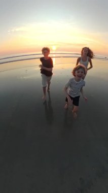 Islak kumsalda, canlı bir günbatımına karşı koşan çocukların 360 'lık görüntüsü, altın parıltıda yakalanan neşeli enerjileri.