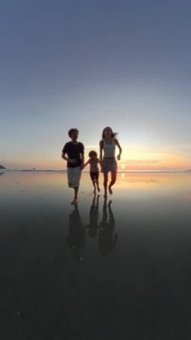 Gün batımında kumsalda el ele koşan çocukların 360 derece neşe dolu görüntüsü, batan güneşin sıcacık parıltısıyla yıkanmış.