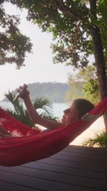 Neşeli bir kız hamakta dinleniyor, kameraya gülümsüyor ve selfie çekiyor, neşe ve sükunetin mükemmel anını yakalıyor.