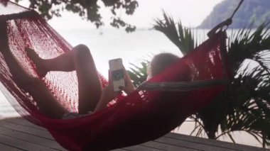 Hamakta uzanmış rahat bir kız gezici fotoğraf düzenleme üzerinde çalışıyor, dışarıda huzurlu bir anın tadını çıkarıyor.