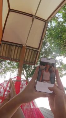 Plaja bakan bir villada hamakta dinlenen bir kızın görüntüsü, sakince akıllı telefonundaki bir fotoğrafı düzenliyor.