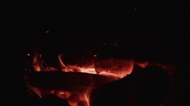 Gece çıtırdayan kamp ateşine bir kütük eklenir, parlak alevlerin yanıp sönmesine ve karanlığın aydınlanmasına neden olur.