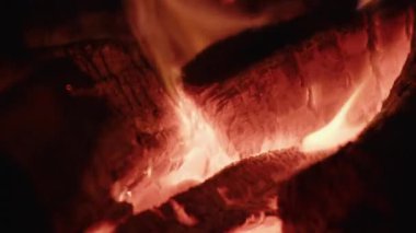 Kamp ateşinde parlak bir şekilde yanan yakacak odunların yakın çekimi sıcak ve büyüleyici bir atmosfer yaratır.