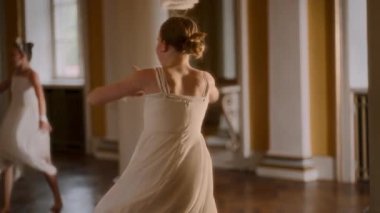 Akan beyaz elbiseli genç bir kız büyük bir balo salonunda çağdaş bir dans gösterisi yaparken kollarını kaldırıp zarif bir şekilde dönüyor.