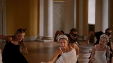 Çağdaş bir dans gösterisinin yoğun bir anı, zarif beyaz elbiseler ve taclar içindeki genç kızlar ön planda anlamlı bir şekilde yürürken, siyah elbiseli dansçılar