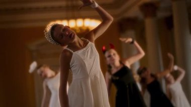 Beyaz elbiseli ve tacı olan genç bir dansçı dengeli ve anlamlı duruşuyla sahneye çıkıyor, zarif hareketleri avizelerin sıcacık parıltısıyla aydınlatılıyor, siyah elbiseli dansçılar ise