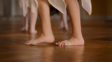 Yakından bakınca, genç dansçıların hareketlerini gösteren büyük, süslü bir balo salonunda dans eden ayaklarını yakalıyor. Parlak ahşap zemin parlak bir zemin sağlar.