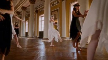 Yüksek sütunları ve altın aksanıyla büyük bir balo salonunda genç dansçılar, beyaz elbiseli ve tacını zarif bir şekilde uzatan bir kız olarak çağdaş bir gösteri sergiliyorlar.