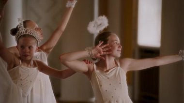 Parlak detaylarla süslenmiş zarif beyaz elbiseli iki genç kız çağdaş bir dans gösterisinden sonra zarifçe poz verirken, ışıl ışıl gülümsemeleri ve etkileyici kol hareketleri