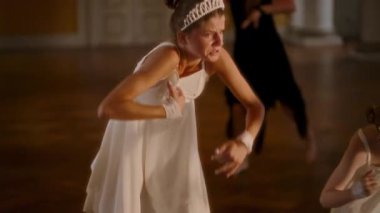 Zarif beyaz elbiseler ve parlak taçlarla iki genç kız etkileyici bir modern dans gösterisi sergiliyorlar. Yoğun odak noktaları ve zarif ama güçlü hareketleri yavaş çekimde çekiliyor.