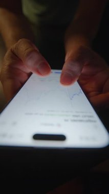 Bir kişinin eli, gerçek zamanlı borsa verilerini ve finansal grafiklerini akıllı telefon ekranında görür