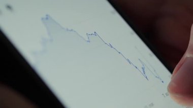 Bir kişi, borsa verilerini izlemek ve mali eğilimleri izlemek için akıllı telefon üzerinde finans uygulaması kullanır