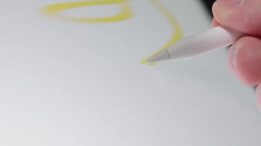 Boş tablet ekranına rastgele sarı çizgiler çizmek için stil kullanan bir elin yakın plan çekimi, dijital yaratıcılık ve teknolojik etkileşim sergiliyor