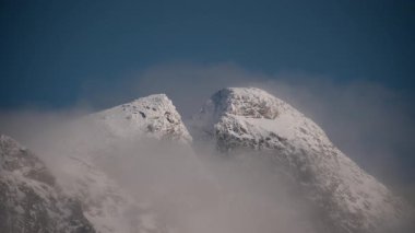Norveç 'in sisli kış dağlarının nefes kesen manzarası. Parlak mavi gökyüzünün altındaki sislerin arasından yükselen karla kaplı tepeler.