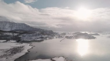 Kuzey kışı manzarasının nefes kesici kuş bakışı görüntüsü, açık gökyüzünün altında donmuş tarlalar ve karla kaplı dağları gösteriyor.
