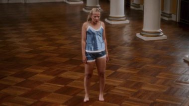 Gece elbisesi giymiş bir dansçının, boş bir dans salonunda etkileyici bir performans sergilediği, zarif ve duygusal bir hareket sergilediği yüksek açılı bir çekim.