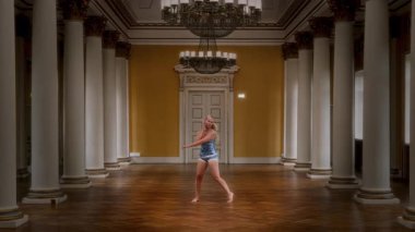Mavi ipek gecelikli yalnız bir kız zarif bir dans salonunda dans ediyor, etrafı mimari sütunlarla çevrili.