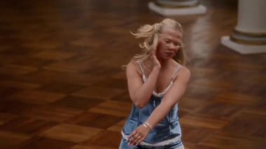 Gecelikli genç kız parke zeminde anlamlı bir şekilde dans ediyor, sıvı ve duygusal hareketler sergiliyor.