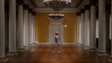 Mavi ipek gecelikli genç dansçı zarif bir dans salonunda parke döşemeli ve etkileyici bir dans sergiliyor.