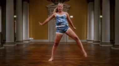 Gecelik giymiş çıplak ayaklı bir dansçı zarif balo salonunda zarif bir şekilde dans ederek duygusal olarak yüklü çağdaş bir dans sergiliyor.