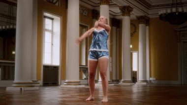 Gecelik giymiş çıplak ayaklı bir kadın zarif, modern bir dans sergiliyor. Zarif bir balo salonunda akıcı bir şekilde kıvrılıp hareket ediyor.