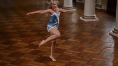 İpek gecelikli zarif çıplak ayaklı kadın parlak ahşap bir dans pistinde piruet yapıyor. Hareketleri akıcı ve zarif.