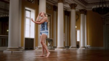 Gecelik giymiş çıplak ayaklı bir kadın etkileyici, zarif bir dans sergiliyor. Büyük bir balo salonunda zarifçe kıvrılıp hareket ediyor.