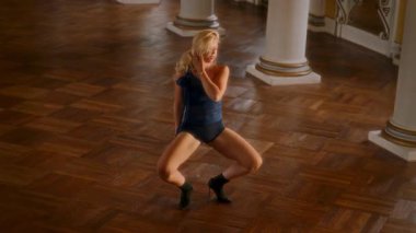 Genç kız yüksek topuklularla, parlak ahşap zeminde anlamlı bir dans sergiliyor, sıvı ve dinamik hareketler sergiliyor