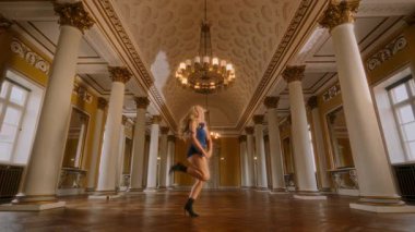 Tek omuzlu genç bir kadın, geniş bir dans salonunda akışkan hareketler ve duygusal derinlik sergileyerek çağdaş bir dans sergiliyor.