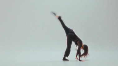 Siyahlı genç kız etkileyici bir ters takla atıyor ve ardından minimalist bir stüdyoda zarif bir dans gösterisi yapıyor.