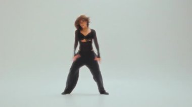 Siyahlı genç kız, minimalist bir stüdyoda akışkan hareketler ve duygular sergileyen çağdaş bir dans sergiliyor.