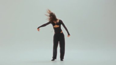 Siyahlı genç bir dansçı, minimalist beyaz bir stüdyoda, akışkan hareketler ve güçlü duygular sergileyen etkileyici bir modern dans gösterisi sergiliyor.
