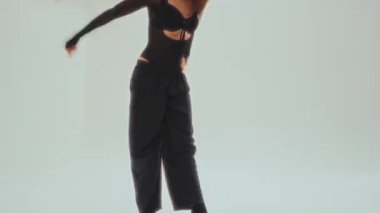 Siyahlı kendinden emin genç bir dansçı, minimalist beyaz bir stüdyoda dinamik bir ters takla atar.