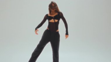 Siyah kıyafetli zarif genç bir dansçı minimalist bir stüdyoda zarif bir dönüş yapıyor, akışkan bir hareket ve mükemmel bir denge sergiliyor.