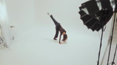 Kendine güvenen genç bir dansçı, minimalist beyaz bir stüdyoda güçlü bir ters takla atar.