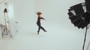 Siyah elbiseli genç bir kız zarif bir dönüş yapıyor. Parlak, minimalist beyaz bir odada. Dans hareketlerinde zarafet ve hassasiyet sergiliyor.